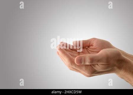 Mani con palme su di un uomo religioso con gesto di offerta con fondo grigio isolato. Vista laterale. Foto Stock