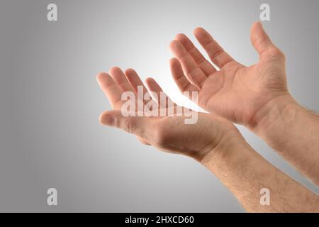 Mani con palme su di un uomo religioso con gesto di chiedere con fondo grigio isolato. Vista rialzata. Foto Stock