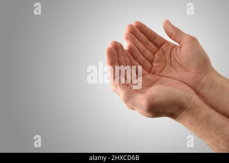 Mani con palme su di un uomo religioso con gesto di offerta con fondo grigio isolato. Vista rialzata. Foto Stock