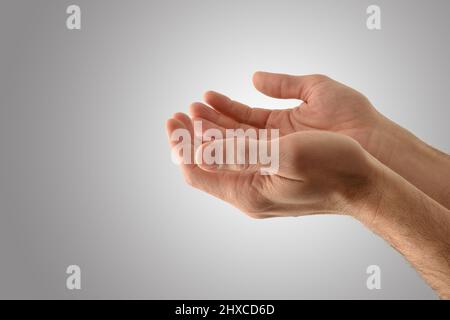 Dettaglio mani con palme su di un uomo religioso con gesto di offerta con fondo grigio isolato. Vista laterale. Foto Stock