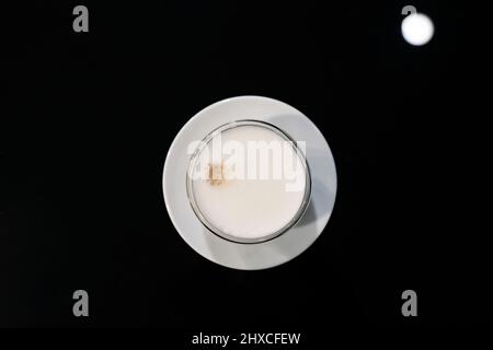 Tazza di cappuccino al caffè con schiuma di schiuma su un tavolo di vetro nero. Vista dall'alto. Foto Stock