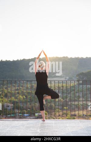 Donna che pratica yoga all'aperto con vista sulla valle Foto Stock