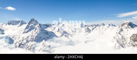 Panorama di montagne sopra le nuvole sotto un cielo limpido in una giornata di sole Foto Stock