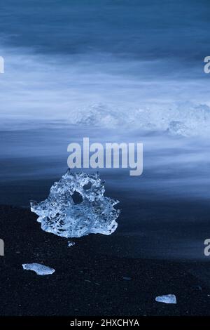 Ghiaccio sulla spiaggia nera vicino alla laguna del ghiacciaio Jökulsárlón, onde a lunga esposizione, atmosfera serale, ora blu, Parco Nazionale Vatnajökull, Islanda Foto Stock