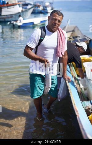 La pesca è la mia vita. Ritratto di un pescatore in piedi in acqua accanto alla sua barca. Foto Stock