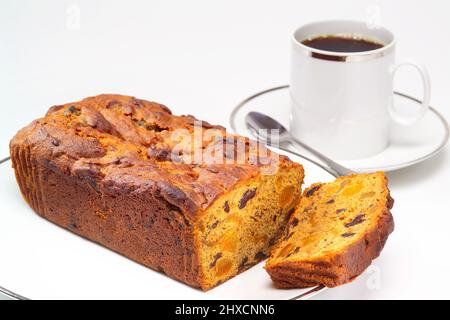 Tazza bianca a faccia diritta con una banda d'argento intorno al bordo contenente caffè nero con una torta di frutta in primo piano. Foto Stock