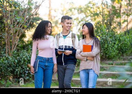 Tre giovani studenti multietnici camminano per strada e parlano Foto Stock