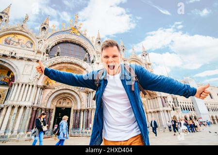 Giovane uomo di stile sorridente che guarda la macchina fotografica in piedi di fronte alla basilica di san marco Venezia, Italia Foto Stock