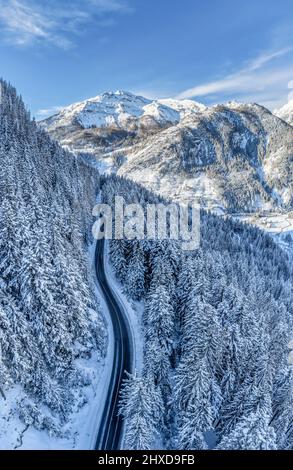 Europa, Italia, Veneto, provincia di Belluno, Dolomiti, strada di montagna che attraversa una foresta di conifere dopo una nevicata, vista dall'alto Foto Stock
