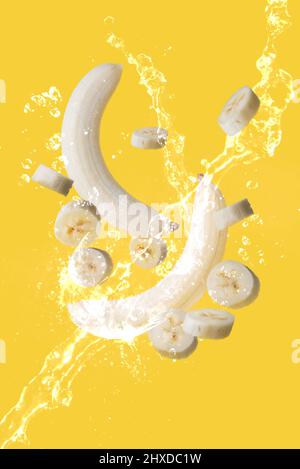 Diverse banane e fette di banana sospese nell'aria e circondate da acqua dolce su sfondo giallo Foto Stock