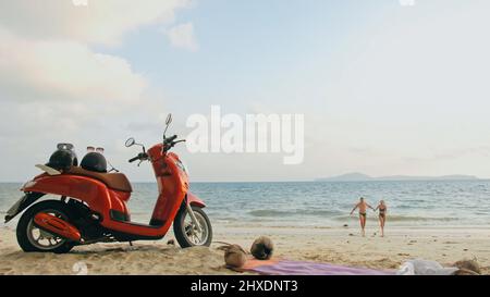Viaggio su strada in scooter. Bella coppia su moto rossa in abiti bianchi sulla spiaggia di sabbia. Appena sposato gente baciare hugs che camminano vicino alle palme tropicali, Foto Stock