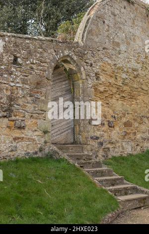 Porta ad arco in un vecchio muro di pietra con cancello di legno su alcuni gradini Foto Stock
