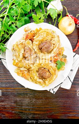 Pasta intrecciata con polpette al centro con salsa di panna, pomodori stufati, peperoni, cipolle e aglio in piatto bianco sul retro del pannello di legno scuro Foto Stock