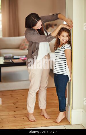 La mia bambina sta crescendo così velocemente. Scatto di una bella madre che misura l'altezza adorabile delle sue figlie a casa. Foto Stock