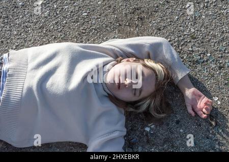 Omicidio sulla strada. Il corpo di una ragazza adolescente in un maglione bianco si trova sull'asfalto sulla strada. Vittima di un incidente stradale. Il concetto di kidn Foto Stock