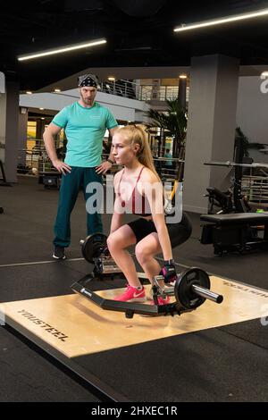 RUSSIA, MOSCA - FEB 11, 2022: Istruttore e cliente ragazza deadlift bionda trappola bar attraente donna, per le istruzioni moderne in trappole dallo sport Foto Stock