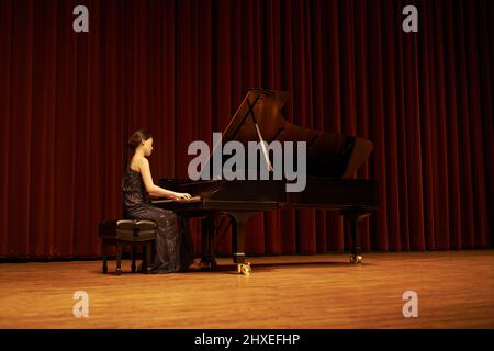 Condividere il suo regalo con la folla. Scatto di una giovane donna che suona il pianoforte durante un concerto musicale. Foto Stock