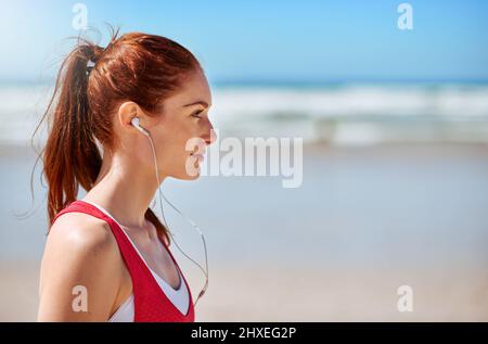 La sua musica che la motiva. Scatto corto di una giovane donna sportiva sulla spiaggia. Foto Stock