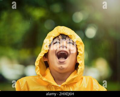 C'è così tanto divertimento da avere sotto la pioggia. Scatto corto di un ragazzo adorabile nella pioggia fuori. Foto Stock