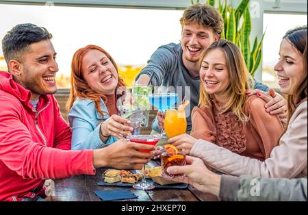 gruppo di amici giovani adulti che si riposano in un bar ristorante all'aperto sul tetto. le persone che si divertono con l'happy hour bevendo alcolici e mangiando si siedono Foto Stock