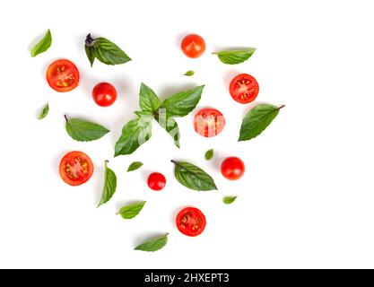 Pomodori e foglie di basilico a forma di cuore isolato su sfondo bianco Foto Stock