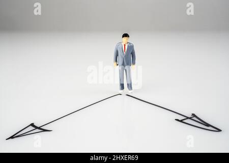 un modello in miniatura davanti alla scelta della direzione da assumere su una superficie bianca Foto Stock