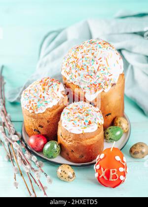 Tradizionale russo ucraino torta di Pasqua Kulich. Pane di Pasqua cristiano ortodosso o torta di Pasqua con glassa, uova di Pasqua e rametti di salice su sfondo blu. Spazio di copia per il testo, verticale Foto Stock