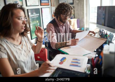 due giovani colleghi caucasici adulti che guardano le statistiche, consultano, lavorano insieme. Concetto di lavoro di squadra Foto Stock