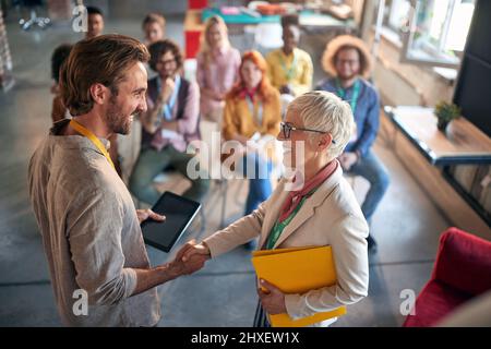 I colleghi si scuotono le mani dopo una presentazione ben fatta in un'atmosfera piacevole in una sala conferenze. Dipendenti, ufficio, lavoro Foto Stock