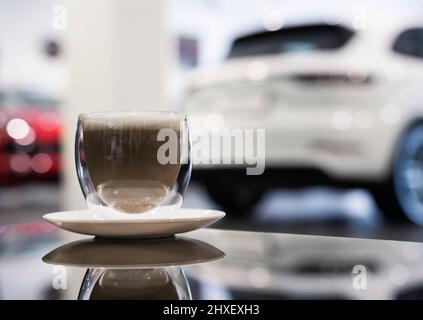 Tazza di caffè cappuccino con schiuma su un tavolo di vetro nero in un concessionario di automobili. Foto Stock