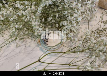 Candele di cera di soia con lavanda in vasetti sullo sfondo della gypsophila fiorente Foto Stock