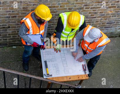 L'architetto con il piano di costruzione in discussione con i supervisori di costruzione. Foto Stock