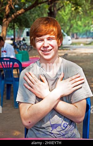 Ragazzo con i capelli rossi e piccone in faccia sembra felice e keepts le braccia incrociate Foto Stock