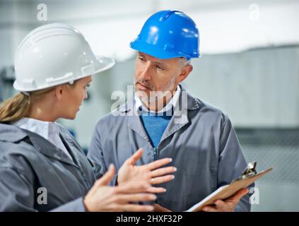 La comunicazione prende pratica. Due dipendenti della fabbrica che indossano i cappelli hanno una discussione. Foto Stock