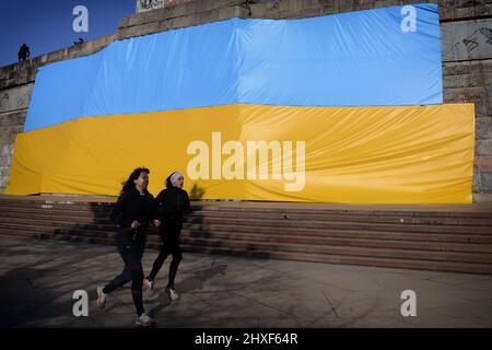 Praga, Repubblica Ceca. 12th Mar 2022. Le donne che fanno jogging intorno a una grande bandiera in colori ucraini, che si trova sul parco Letna a Praga, nella Repubblica Ceca. (Credit Image: © Slavek Ruta/ZUMA Press Wire) Credit: ZUMA Press, Inc./Alamy Live News Foto Stock