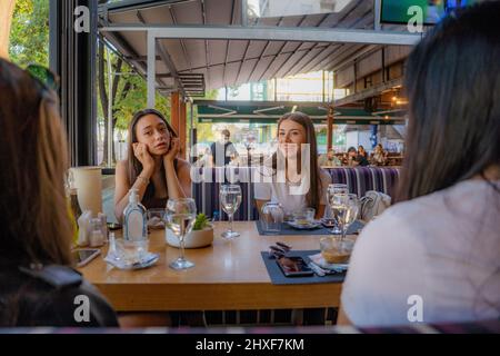 Quattro ragazze attraenti e belle stanno sorridendo circa i ragazzi dietro loro mentre parlano di loro Foto Stock