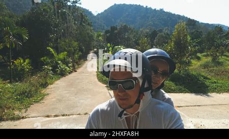 Due turisti caucasici uomo guida su scooter rosso. Renderla selfie. Coppia d'amore in moto in abiti bianchi per andare sulla strada forestale viaggio. Motore Foto Stock