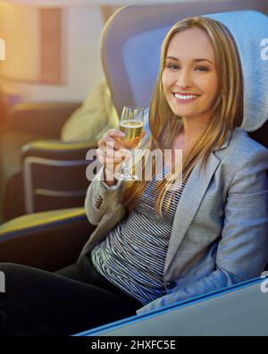 Volare con stile. Ritratto di una giovane donna che beve champagne in prima classe su un aereo. Foto Stock