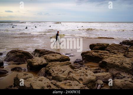 I surfisti si fanno strada in mare a Rest Bay a Porthcawl mentre un avvertimento vento giallo è in vigore in tutto il Galles occidentale durante il fine settimana. Data foto: Sabato 12 marzo 2022. Foto Stock