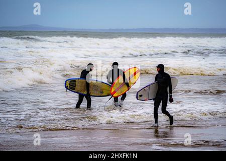 I surfisti si fanno strada in mare a Rest Bay a Porthcawl mentre un avvertimento vento giallo è in vigore in tutto il Galles occidentale durante il fine settimana. Data foto: Sabato 12 marzo 2022. Foto Stock