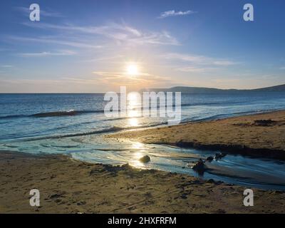 Un sole che scende, dirigendosi verso il promontorio, getta un percorso dorato che si intravede attraverso le acque di Solent fino alla spiaggia sabbiosa di Compton Bay. Foto Stock