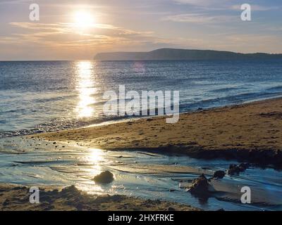 Un sole che scende, dirigendosi verso il promontorio, getta un percorso dorato che si intravede attraverso le acque di Solent fino alla spiaggia sabbiosa di Compton Bay. Foto Stock