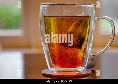 Estrazione della bustina di tè in acqua - caffeina bevanda in tazza di tè con pareti in vetro doppio - primo piano di un teabag parzialmente preparato in un teacup di acqua calda Foto Stock