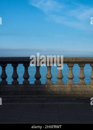 Un cielo costiero sopra una balaustra ornamentale su una spianata di parete del mare in un faretto di luce del sole che mette in risalto le ombre. Foto Stock