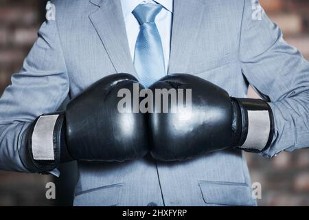 Hell combattere la sua strada verso l'alto. Un uomo in un vestito che pugni i suoi guanti da boxe insieme. Foto Stock