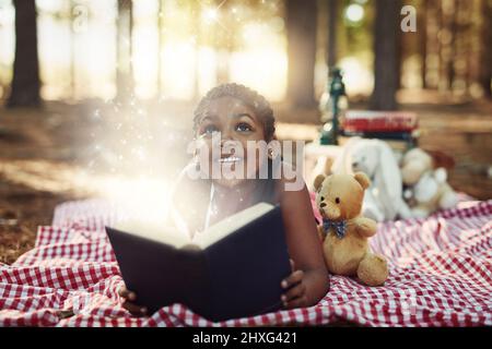 Lasciate che la lettura vi porta in un mondo magico e meraviglioso. Shot di una bambina che legge un libro con pagine incandescenti nei boschi. Foto Stock