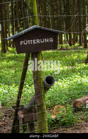 Segno 'Fütterung' ('alimentazione') e dispositivo di alimentazione sul recinto di un recinto di gioco. Foto Stock