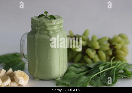 Frullato verde a base di uva verde congelata, spinaci freschi, banane e latte di mandorle. Servito in vasetto di mason. Scatto su sfondo bianco. Foto Stock