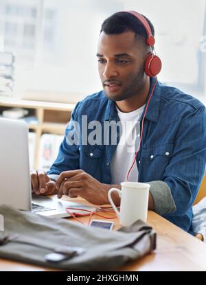 Godendo della musica che lavora. Un bel uomo d'affari vestito casualmente che lavora nel suo ufficio. Foto Stock