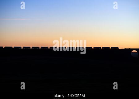 Treno merci trasporto passando in pietra Ribblehead sul Settle - Carlisle linea facendo una silhouette al tramonto Foto Stock